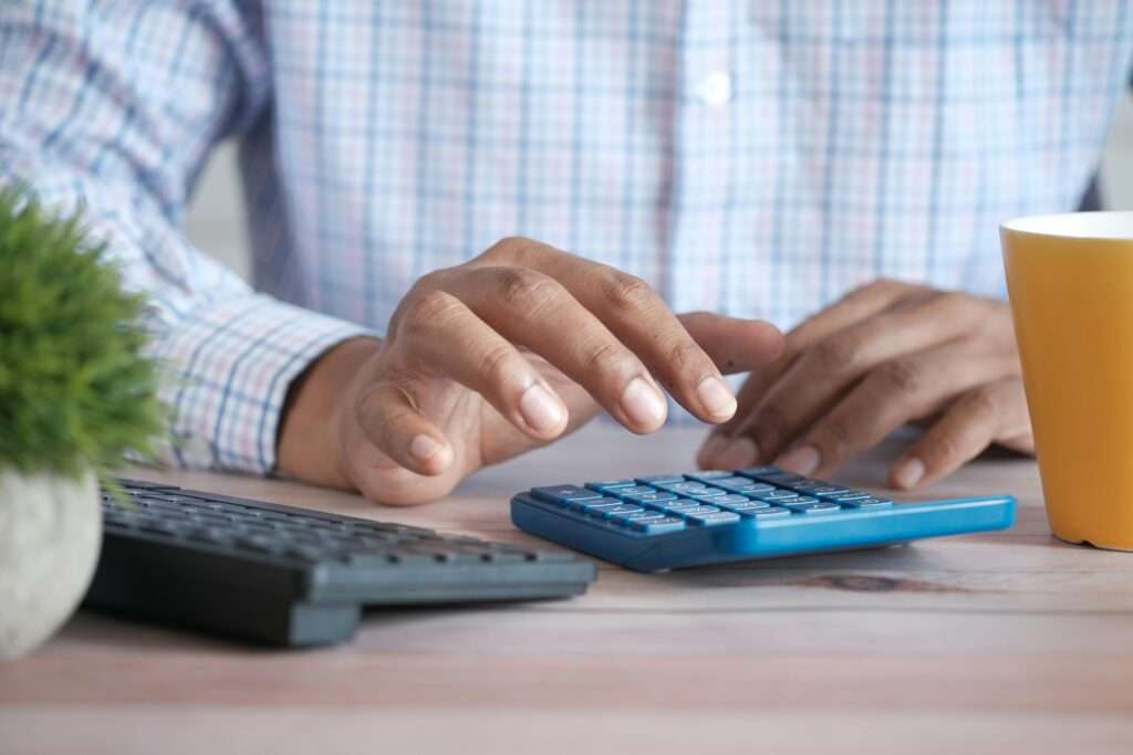 A man in front of a calculator and keyboard calculating female speaker fees.