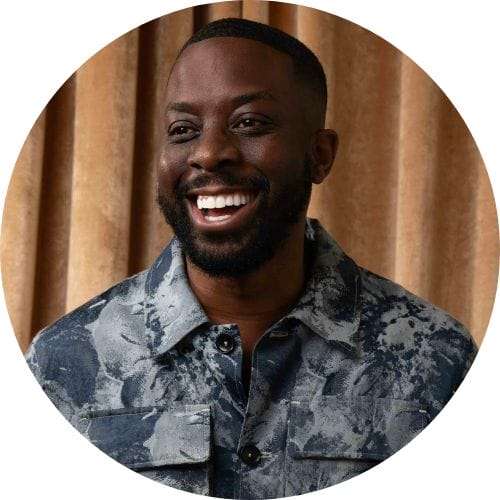 A black man smiling in a camouflage shirt.