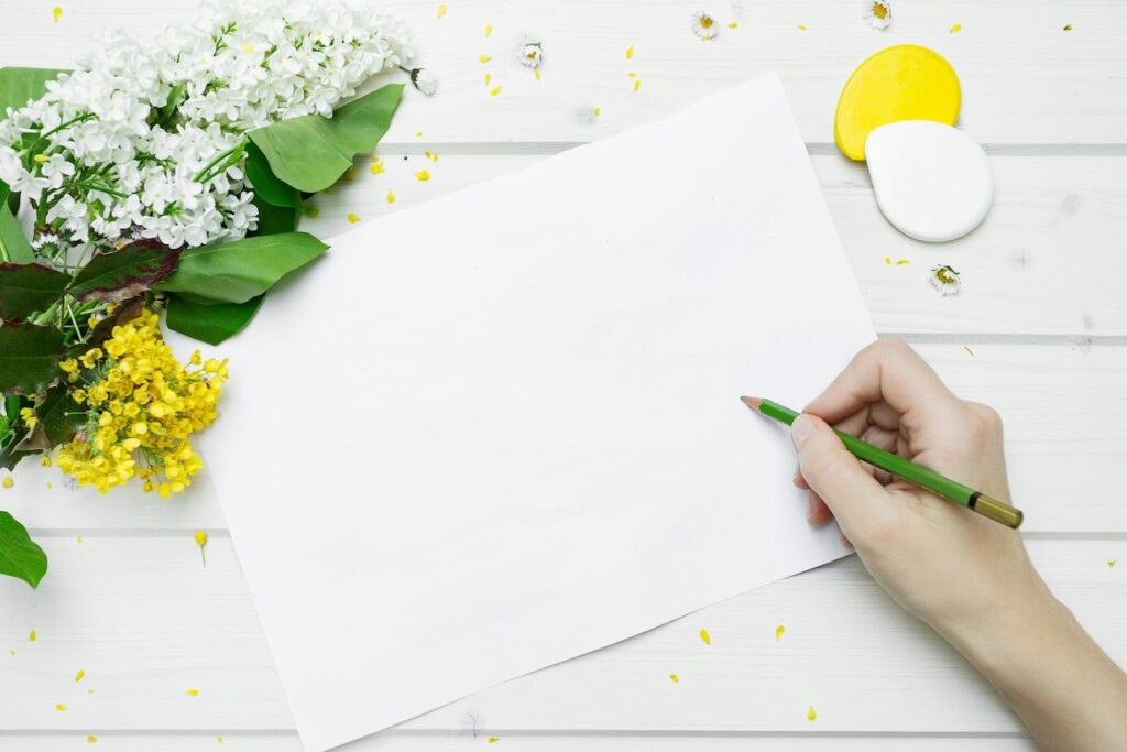 A hand holding a pencil over a white paper with yellow flowers